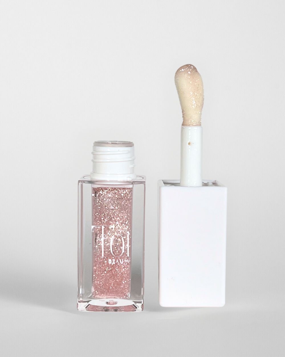 A clear tube with a white cap containing a pink lip oil, alongside a applicator wand with a sponge tip for dry lips. Color Angel